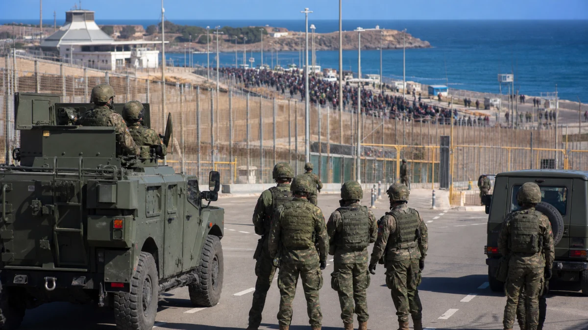 Spanische Soldaten und Militärfahrzeuge an der Grenzanlage von Ceuta, im Hintergrund eine große Menschenmenge