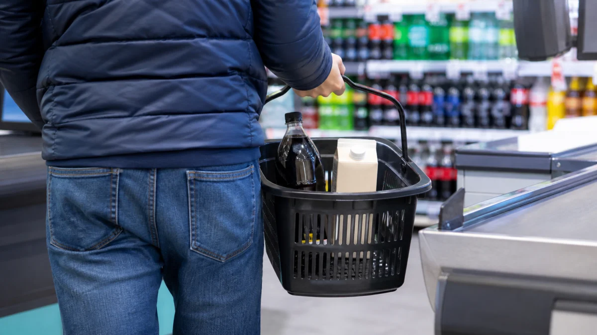 Kunde mit Getränken in einem Einkaufskorb an einer Supermarktkasse.