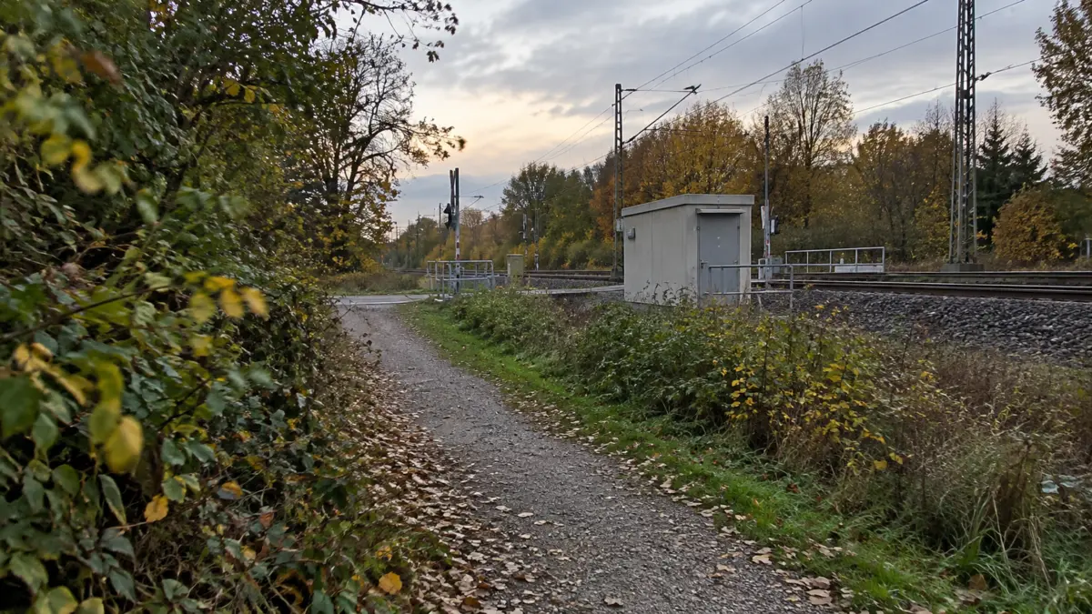 Kiesweg an Bahngleisen und Bahnübergang mit Büschen am Rand