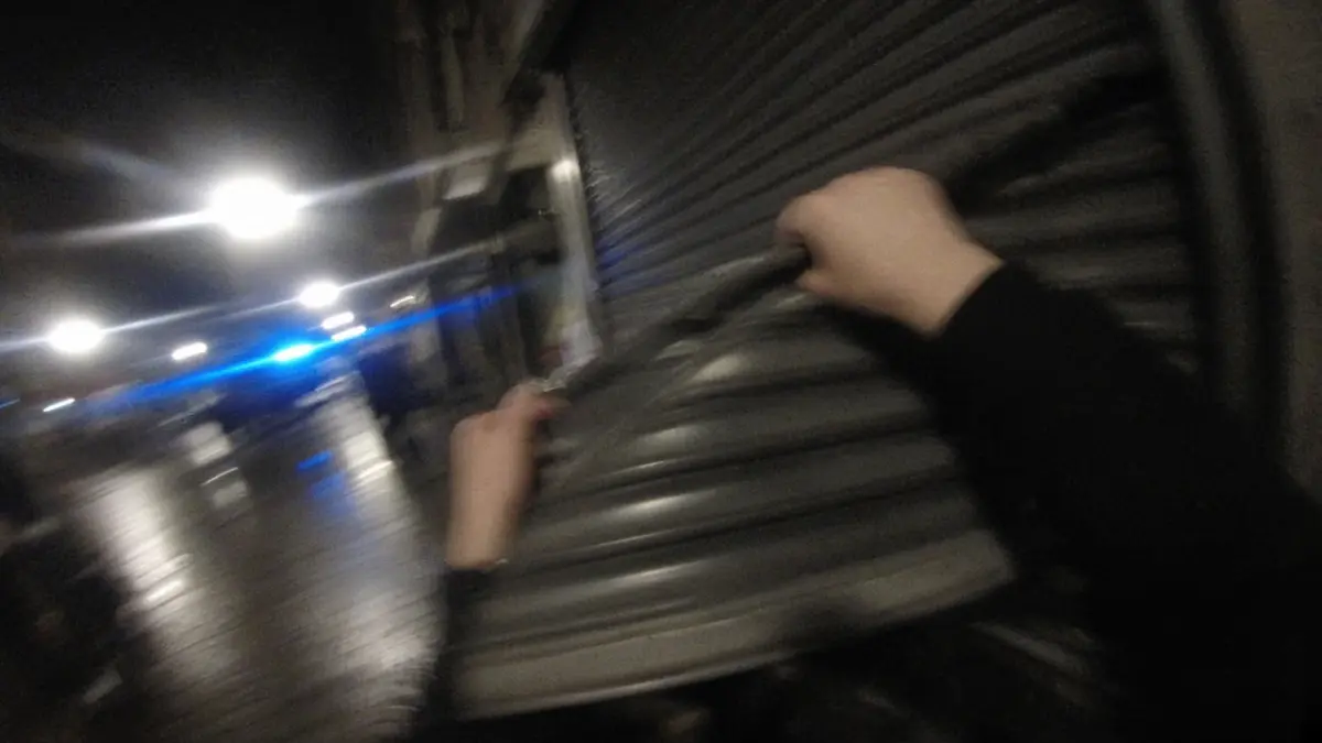 Symbolbild: Hände ziehen nachts einen Rollladen herunter, Blaulicht im Hintergrund