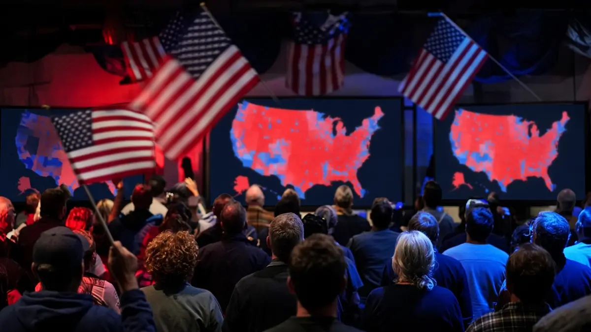 Menschenmenge von hinten vor großen Bildschirmen mit rot-blauer USA-Karte in Wahlnachtstimmung, Flagge mit Bewegungsunschärfe