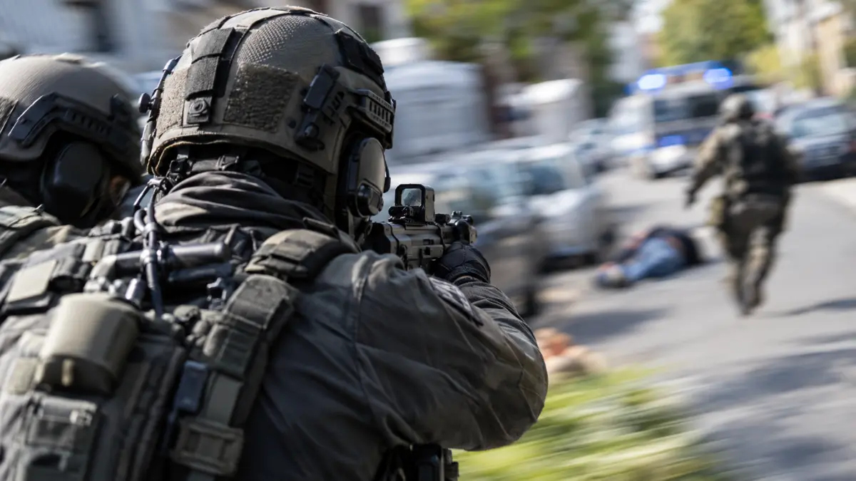 SEK-Beamte von hinten mit Schusswaffe im Anschlag, im unscharfen Hintergrund liegt ein Verletzter