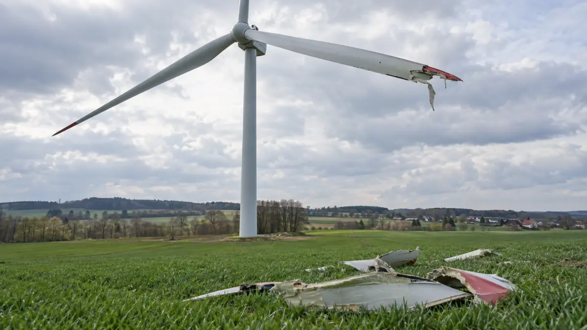 Beschädigter Flügel eines Windrads über einem Feld